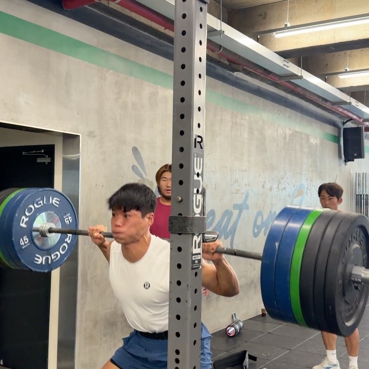 A front squat in a Rogue rack, the Sweat on Seoul lettering behind