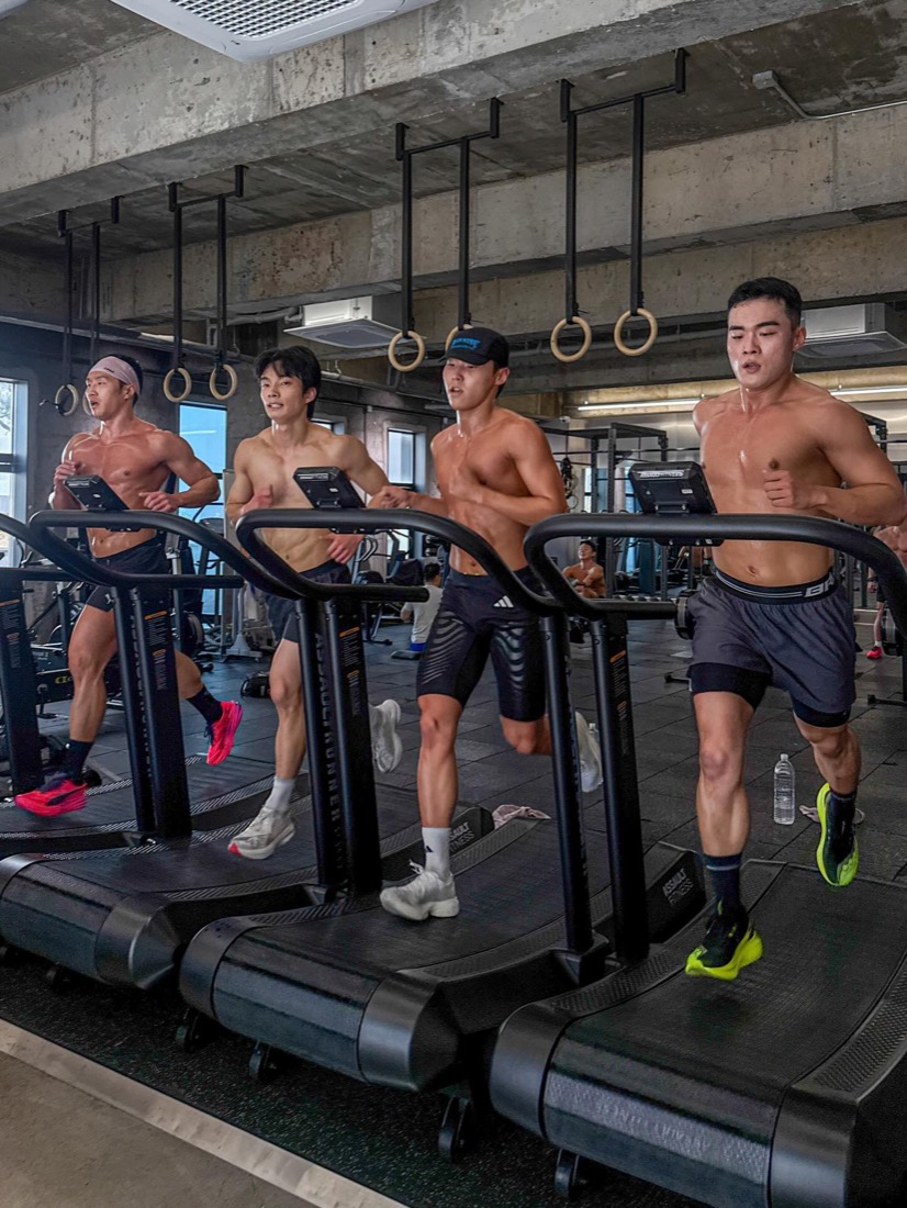 Four people running on curved treadmills under gymnastic rings